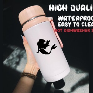 May include: White insulated water bottle with a pink lid and a black silhouette of a mermaid on the side. The bottle has the text "HIGH QUALITY WATERPROOF EASY TO CLEAN NOT DISHWASHER SAFE" printed on the side.