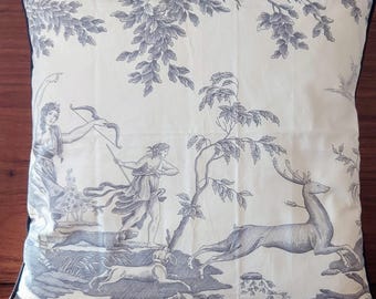 May include: A white throw pillow with a black and white toile pattern featuring a woman with a bow and arrow, a deer, and trees.
