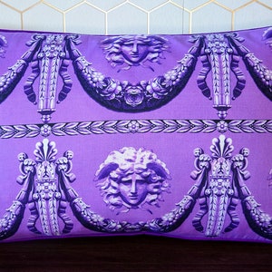 May include: Purple pillow with a repeating pattern of a woman's face with snakes in her hair, ornate floral designs, and a decorative border.