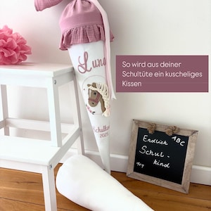 Könnte beinhalten: Eine weiße und rosa Schultüte mit einer Pferdeillustration und dem Namen "Luna". Die Tüte ist mit einer rosa Rüsche und Schleife verziert. Ein passendes Kissen liegt daneben. Der Text auf der Tüte lautet "Schulkind 2025".