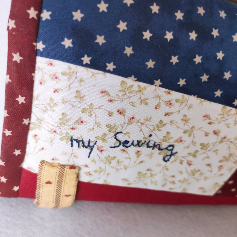 May include: A white fabric with a floral pattern and the words "my Sewing" embroidered in blue thread. The fabric is surrounded by red and blue fabric with white stars.