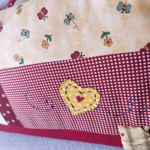 May include: A red and white checkered fabric with a yellow heart with white polka dots and a red heart in the center. The heart is stitched with blue thread. The fabric has a white star in the corner.