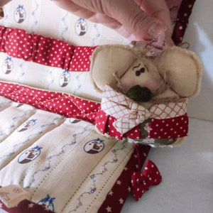 May include: A red and white quilted fabric organizer with a small stuffed mouse with a red and white checkered scarf. The mouse is holding a green button in its paws.