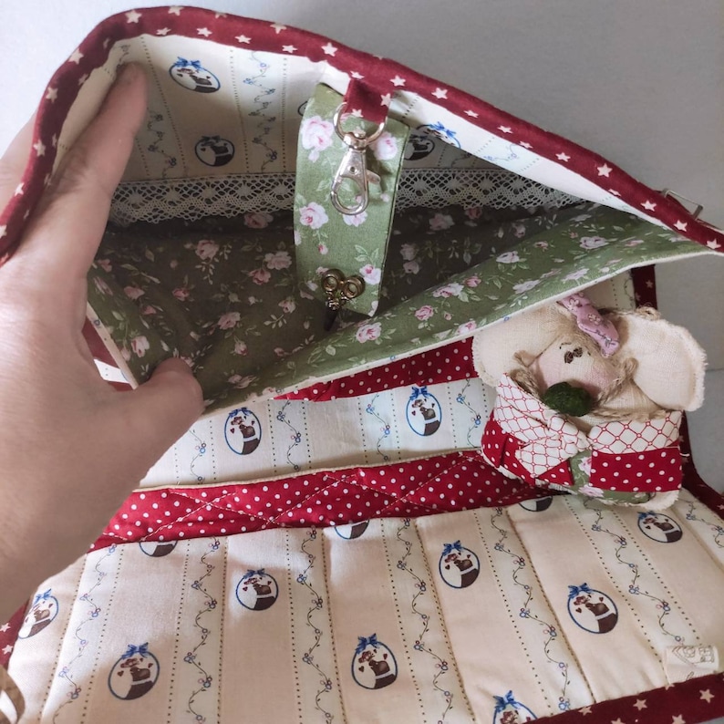 May include: A red and white quilted fabric bag with a green floral lining. The bag has a zipper closure and a small pocket on the inside. A small stuffed animal is inside the bag.