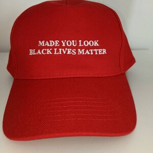 Può includere: Un berretto da baseball rosso acceso con la scritta bianca ricamata "MADE YOU LOOK BLACK LIVES MATTER". Il berretto ha una visiera curva e una corona strutturata, adatto per l'uso casual.