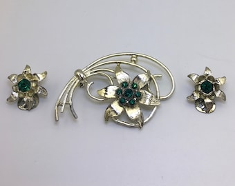 Conjunto de joyería, broche y pendientes de clip, broche de flor en tono dorado con piedras redondas verde esmeralda en el centro y pendientes de clip a juego.