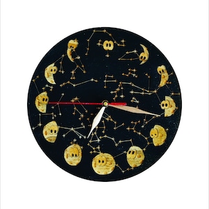 May include: A black circular clock with a white hand and a red hand. The clock face features a design of gold moons and stars.