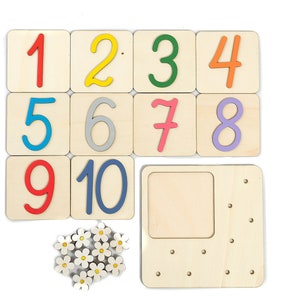 May include: Wooden number tiles with colorful numbers 1 through 10. The tiles are arranged in three rows. There is a wooden frame with a blank space and holes around the edge. There are also small white wooden flowers with yellow centers.