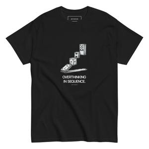 Könnte beinhalten: Schwarzes T-Shirt mit einer Grafik von fallenden Dominosteinen in Sequenz und dem Text "OVERTHINKING IN SEQUENCE." Das T-Shirt hat einen Rundhalsausschnitt und kurze Ärmel. Der Markenname "BETWEENE" ist oben aufgedruckt.