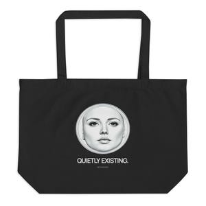 以下が含まれることがあります： 黒いトートバッグ。円の中に女性の顔の白黒ポートレートが描かれています。「QUIETLY EXISTING.」の文字が下に印刷されています。バッグには2つの黒いハンドルが付いています。