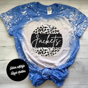 May include: A blue and white bleached t-shirt with a circle design featuring a leopard print and the word "Jackets" in black with glitter. The shirt is a Gildan softstyle in Royal Heather.