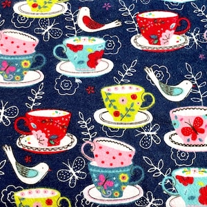 May include: A navy blue fabric featuring a repeating pattern of colorful teacups, saucers, and birds. The teacups are decorated with floral and butterfly designs in shades of red, pink, yellow, and teal. White floral and butterfly outlines are scattered across the background.