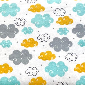 Könnte beinhalten: Weißer Stoff mit einem sich wiederholenden Muster aus stilisierten Wolken. Die Wolken sind in Blau-, Gelb-, Grau- und Weißtönen gehalten, mit kleinen grauen Punkten. Die Wolken haben ein skurriles, cartoonartiges Design.