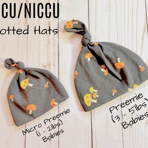 May include: Two gray knotted hats with a mushroom print. The smaller hat is labeled "Micro Preemie (1-2 lbs) Babies" and the larger hat is labeled "Preemie (3-5 lbs) Babies".