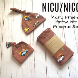 May include: A brown baby set comprising two knotted hats and a swaddling blanket. The set is decorated with a repeating pattern of small cars and trees. The text "NICU/NICCU Micro Preemie Grow into Preemie Set" is visible.