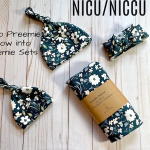 Puede incluir: Un conjunto de artículos para bebés, que incluye dos gorros anudados, una diadema y una manta envolvente. Los artículos son de color verde azulado oscuro con un estampado floral blanco. El texto incluye "NICU/NICCU" y "Micro Preemie Grow into Preemie Sets".