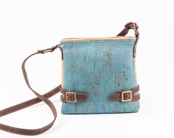 May include: A blue and beige cork crossbody bag with brown leather straps and gold buckles.