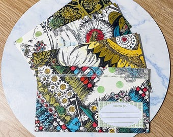 May include: A set of four colorful envelopes with a floral and botanical design. The envelopes have a white background with green, red, blue, and yellow flowers and leaves. The envelopes have a label that says "Deliver to:" and a blank space for writing an address.