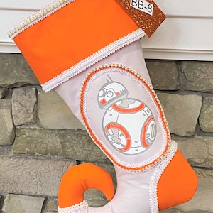May include: Orange and white Christmas stocking with a white BB-8 character from Star Wars. The stocking has gold trim and a tag that says "BB-8".