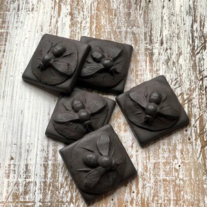 May include: Five black ceramic tiles with raised designs of bees. Each tile features a different bee design with intricate details.