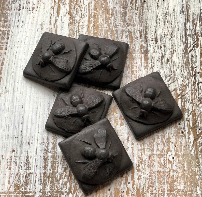 May include: Five black ceramic tiles with raised designs of bees. Each tile features a different bee design with intricate details.