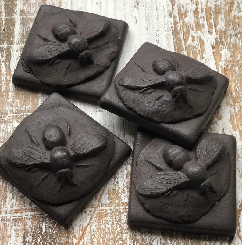 May include: Four square black ceramic tiles with a raised design of a stylized bee on each tile.