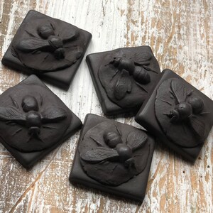 May include: Five black ceramic tiles with raised, detailed images of bees. Each tile has a different bee design.