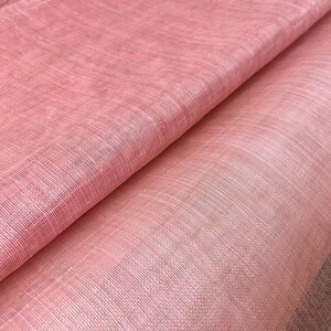 May include: Close-up of folded, light pink fabric with a woven texture. The fabric has a subtle sheen and varying shades of pink, creating depth. The material appears soft and lightweight, suitable for apparel or home decor.