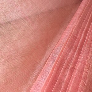 May include: Close-up of a roll of pink fabric. The fabric has a woven texture and a slight sheen. The colour is a soft, muted pink, with subtle variations in tone. The fabric is folded in a pleated style.