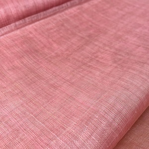 May include: A roll of pink fabric with a woven texture. The fabric is a light, dusty rose colour and appears to be lightweight. The weave is visible, creating a grid-like pattern. The fabric is likely used for clothing or home decor.
