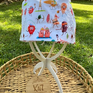 May include: White surgical scrub cap with a colorful pattern of cartoon organs engaged in various sports activities. The cap is displayed on a white stand, with a wooden tag that reads "XNZ Handmade with Love".