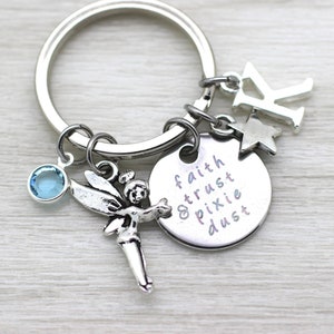 May include: Silver keyring with a charm that says "faith trust pixie dust" and a small fairy charm with a blue crystal. The keyring also has a silver letter K charm and a star charm.