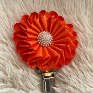 May include: Orange satin flower with a pearl centre attached to a silver clip.