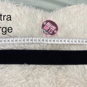 Pode incluir: Coleira preta extra grande para animais de estimação com uma fita métrica mostrando seu comprimento. A coleira é colocada em uma superfície branca e fofa. O texto "Extra Large" é visível. Um adesivo redondo com o texto "Buscador Gifts" também é visível.