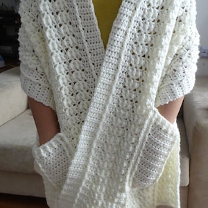 May include: White crochet shawl with two pockets, featuring a star fish stitch pattern. The shawl is worn by a person with a yellow shirt underneath. The text "Star Fish Stitch Pocket Shawl" and "www.MeladorasCreations.com" is visible at the bottom of the image.