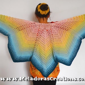 Puede incluir: Un chal de ganchillo arcoíris con un degradado de color turquesa, azul, verde, amarillo, naranja y rosa. El chal está drapeado sobre los hombros de una persona.