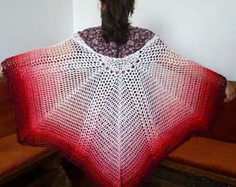 May include: A white crochet poncho with a red and white ombre design. The poncho is made with a loose, open stitch and has a wide, flowing shape.
