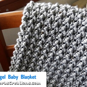 May include: A gray crocheted baby blanket with a textured stitch pattern. The blanket is draped over a wooden chair. The text "Raspberry Angel Baby Blanket" is visible in the lower left corner of the image.
