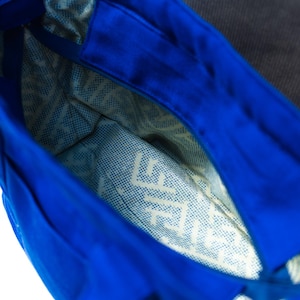 May include: A bright blue tote bag with a wide open top, featuring a light-colored interior lining decorated with a repeating dark blue geometric pattern and the visible text "LIFE" printed on the bottom panel of the bag.