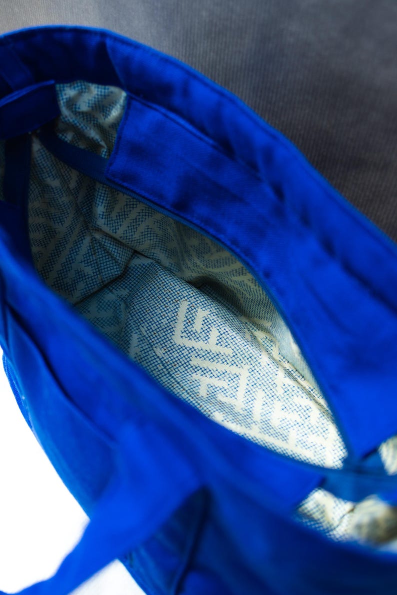 May include: A bright blue tote bag with a wide open top, featuring a light-colored interior lining decorated with a repeating dark blue geometric pattern and the visible text "LIFE" printed on the bottom panel of the bag.