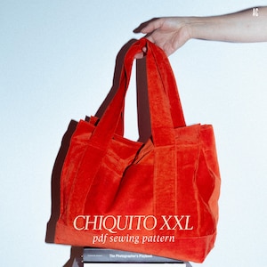 May include: A large, vibrant orange tote bag with long handles, held by a hand. The bag is made of a soft, velvety material. Text on the bag reads "CHIQUITO XXL pdf sewing pattern". The bag is sitting on top of a stack of books.