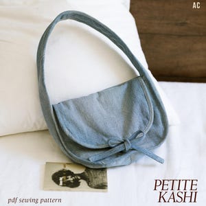May include: A light blue denim shoulder bag with a curved design and a bow closure. The bag has a long strap and a flap that covers the front. The text "PETITE KASHI" and "pdf sewing pattern" are visible.