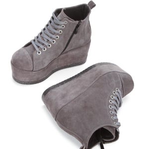 Könnte beinhalten: Graue Wildleder-Plateau-Sneaker mit Keilabsatz. Die High-Top-Schuhe haben graue Schnürsenkel, einen seitlichen Reißverschluss und eine runde Spitze. Die Plateausohle hat einen glitzernden Rand.