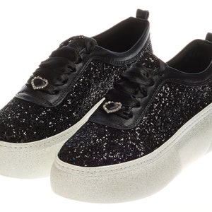 May include: A pair of black glitter platform sneakers with a white sole and a heart-shaped rhinestone embellishment on each shoe.
