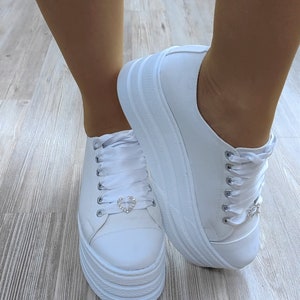 May include: White platform sneakers with white satin laces and a small rhinestone heart detail on each shoe.