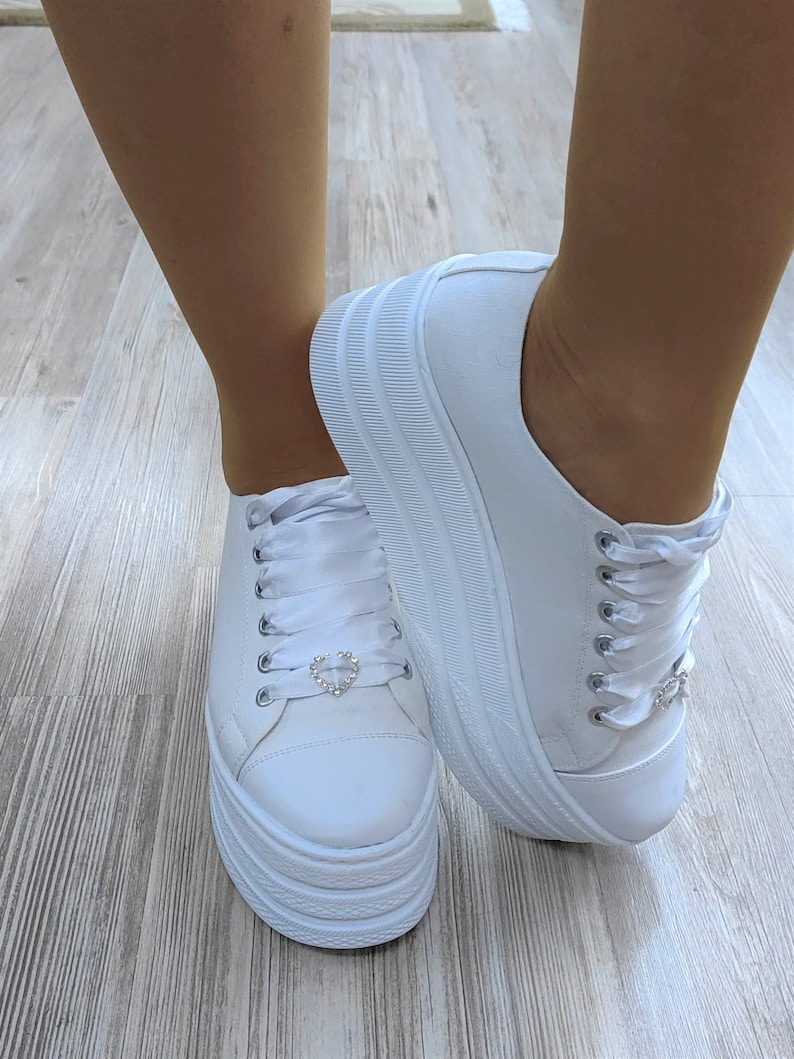 May include: White platform sneakers with white satin laces and a small rhinestone heart detail on each shoe.