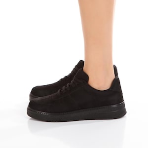 May include: Black suede low-top sneakers with a white rubber sole. The sneakers have a lace-up closure and a rounded toe.