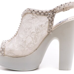May include: White lace platform heels with a rhinestone and pearl embellishment on the strap. The heels are open-toe and have a chunky heel.