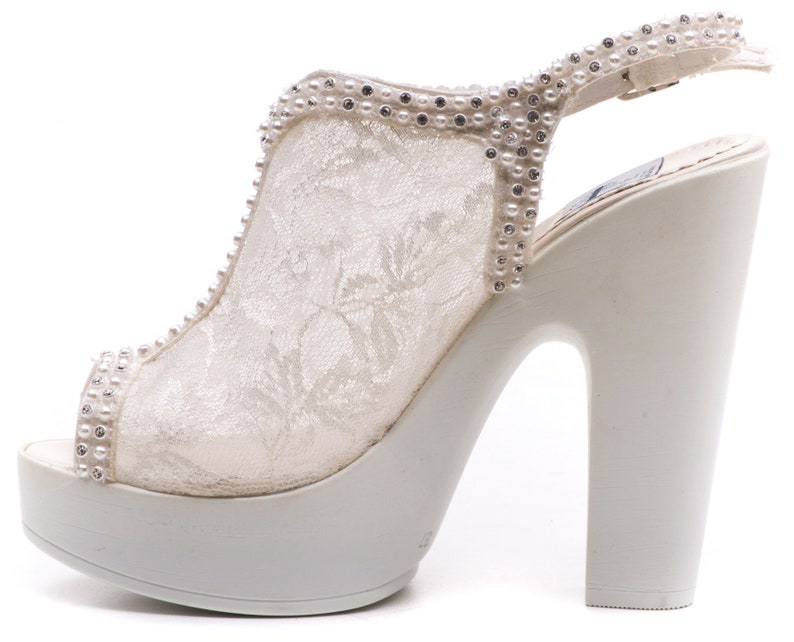 May include: White lace platform heels with a rhinestone and pearl embellishment on the strap. The heels are open-toe and have a chunky heel.