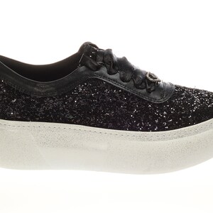 May include: Black glitter sneakers with a white platform sole. The sneakers have a black ribbon lace and a small silver charm on the side.